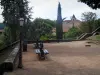 Figeac - Poste de luz e bancos no jardim da igreja de Notre-Dame-du-Puy com vista para as árvores e casas da cidade velha, Quercy