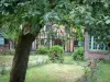 Gerberoy - Garden of a half-timbered house featuring a tree, rosebushes (red roses) and shrubs
