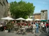 Gordes - Place du village avec terrasses de cafés, parasols, arbres et maisons