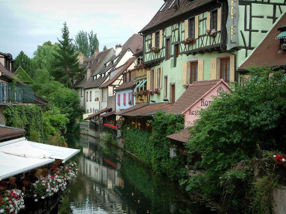 Guide du Grand Est - Colmar - La Petite Venise : rivière (la Lauch) avec maisons à colombages aux façades colorées, arbres et terrasse de café