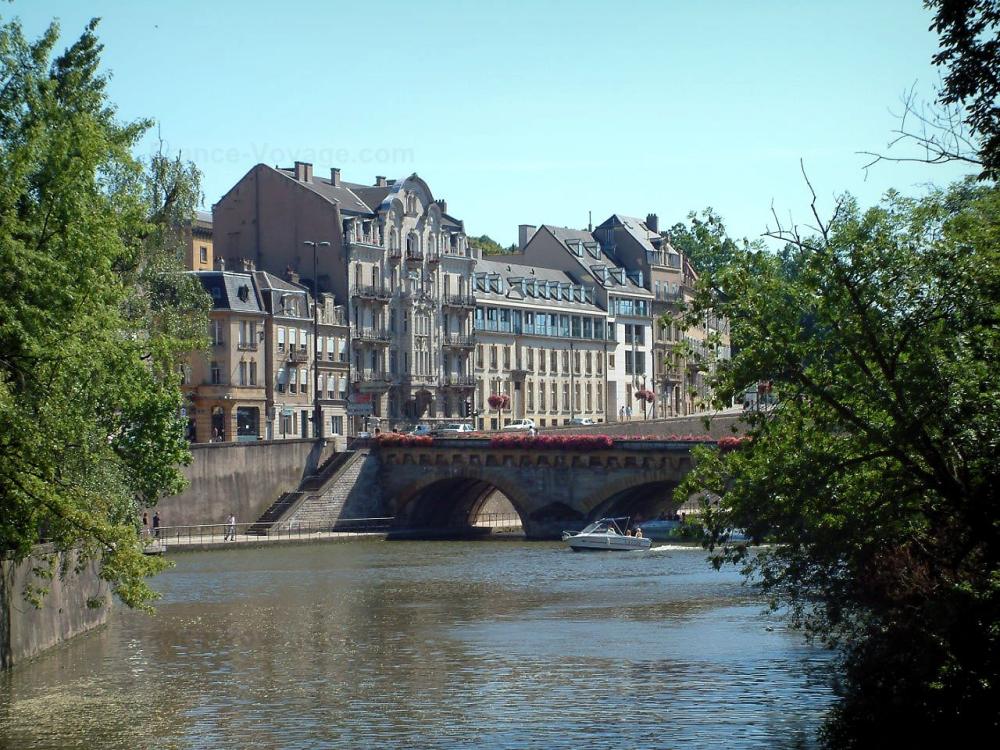 Guide du Grand Est - Metz - Rivière (Moselle) avec bateaux, pont fleuri, arbres et bâtiments
