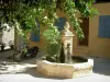 Grimaud - Petite place agrémentée d'une fontaine et d'un arbre, maison de couleur jaune en arrière-plan