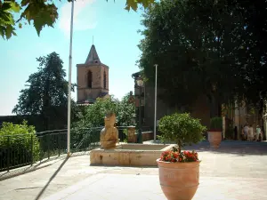 Grimaud - Place agrémentée d'une fontaine et d'arbustes en pots, arbres et clocher de l'église Saint-Michel