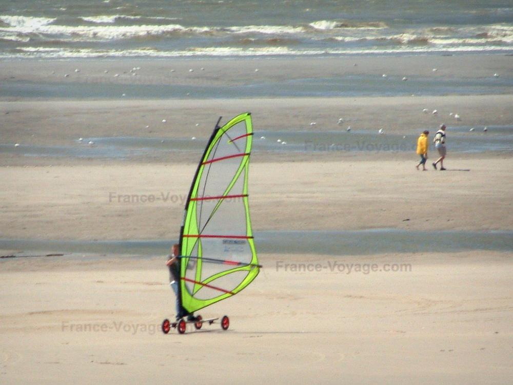 Guide des Hauts-de-France - Hardelot-Plage - Côte d'Opale : plage de sable avec une personne pratiquant le speed-sail (planche à voile sur roulettes), deux promeneurs, des mouettes et la mer (la Manche) ; dans le Parc Naturel Régional des Caps et Marais d'Opale