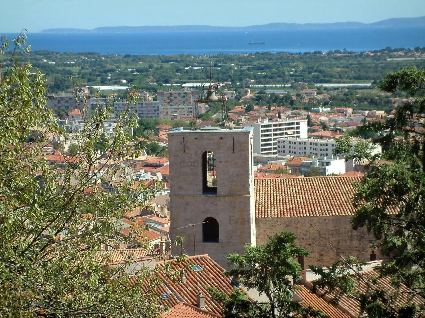 Hyères - Visualizza degli alberi, il campanile romanico della chiesa di Saint-Paul, i tetti delle case e degli edifici della città, la costa e sul Mar Mediterraneo sullo sfondo