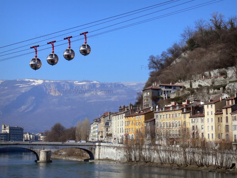 Guide de l'Isère - Grenoble - Bulles du téléphérique de Grenoble Bastille, façades de maisons, pont enjambant la rivière Isère, arbres et montagnes