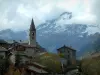 Lanslevillard - Clocher de l'église et maisons du village, montagne enneigée en arrière-plan et ciel nuageux, en Haute-Maurienne (zone périphérique du Parc National de la Vanoise)