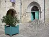 Lauzerte - Canto elevado Place des Cornières, com portal da igreja Saint-Barthélemy, casa com arcade e arbusto florido em pote