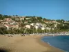 Le Lavandou - Plage de sable avec des estivants, mer méditerranée, palmiers, maisons et immeubles de la station balnéaire