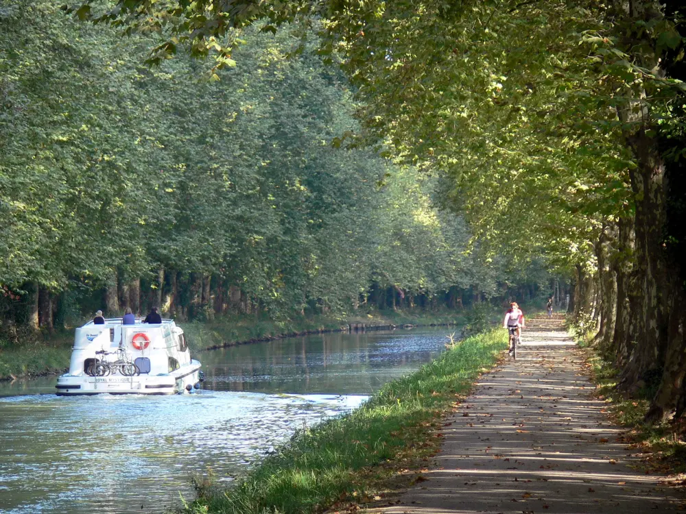 Guide of the Lot-et-Garonne - Greenway of the Garonne canal - Bicycle lane of the Voie Verte greenway with cyclists, plane trees (trees), and boat sailing on the Garonne canal; in Damazan