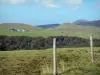 Massif du Sancy mountains - Monts Dore: fence a pasture in foreground, view of trees, a farm and hills covered with grass; in the Auvergne Volcanic Regional Nature Park