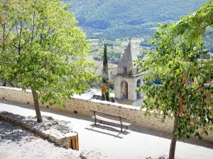 Montbrun les Bains - Banco cercado por árvores com vista para a torre da igreja e a paisagem verde ao redor
