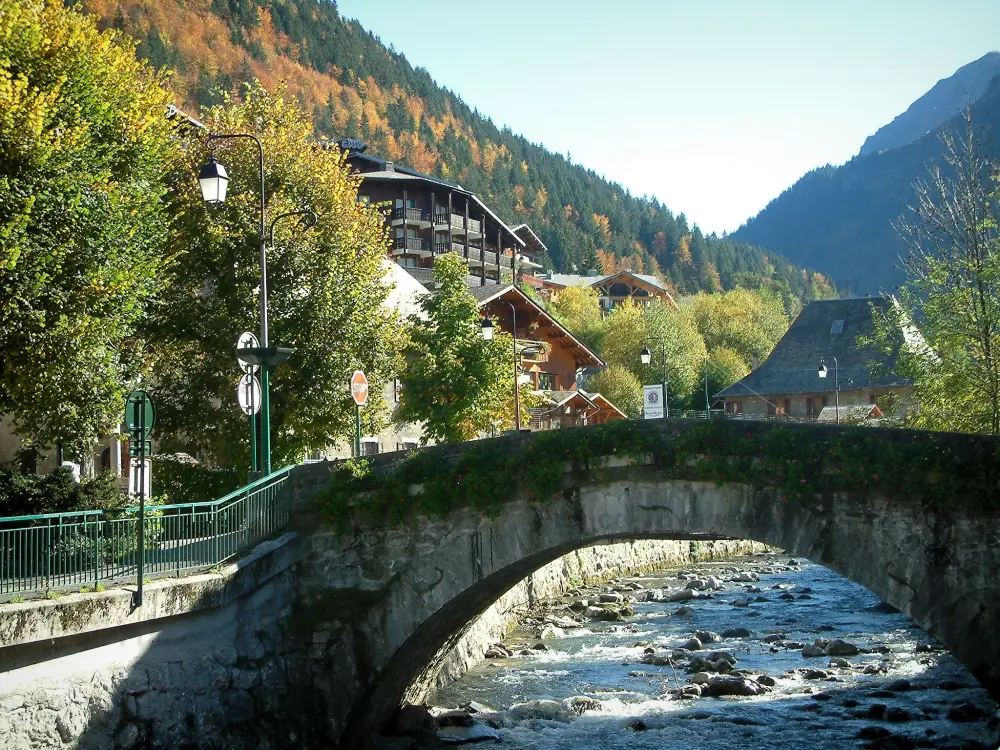 Morzine - Brücke überspannt den Wasserlauf, Bäume, Strassenleuchten und Chalets des Dorfes (Sommer- und Wintersportort), Wald im Herbst, im Haut-Chablais