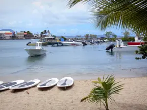 Le Moule - Boards of the canoeing station standing on the sand and fishing port with its moored boats