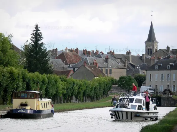 Nivernais canal - Leisure boat sailing on the Nivernais canal, line of trees, bell tower of the Saint-Jean-Baptiste church, and houses of the village of Châtillon-en-Bazois