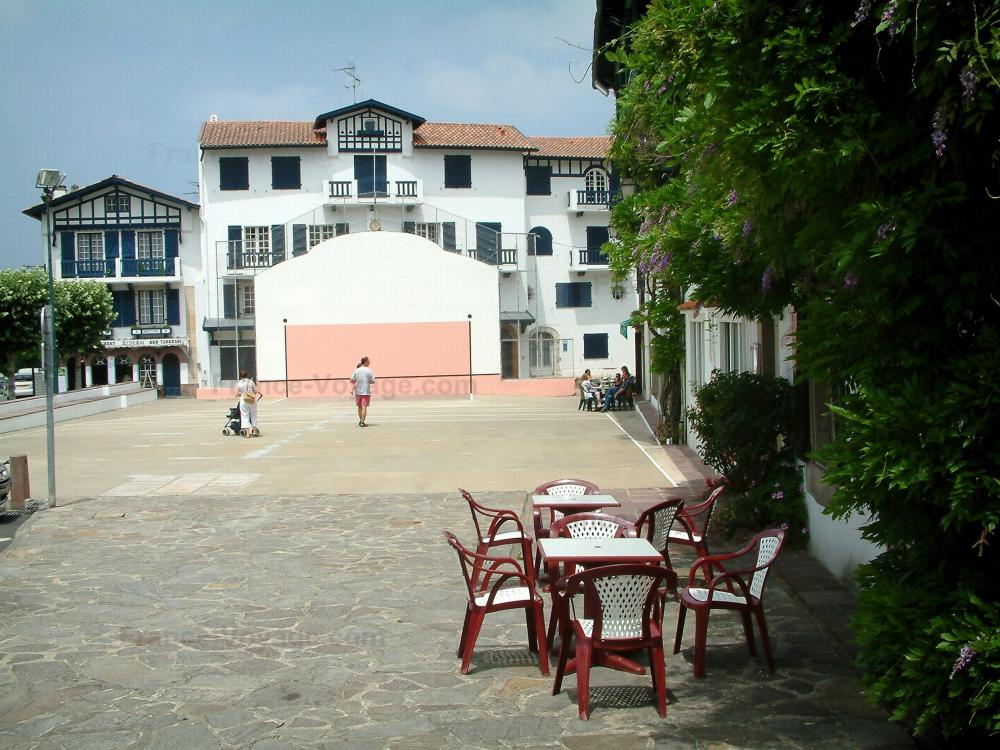 Guide de Nouvelle-Aquitaine - Ascain - Terrasses de cafés, fronton de pelote basque et maisons labourdines