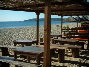 Pampelonne beach - Bay of Pampelonne in Ramatuelle: sandy beach, benches and wooden tables of the bar, the Mediterranean Sea and the Camarat cape