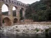 Pont du Gard bridge - Roman aqueduct (ancient monument) with three levels of arcades (arches), bank lined with trees and River Gardon; in the town of Vers-Pont-du-Gard