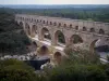 Pont du Gard bridge - Roman aqueduct (ancient monument) with three levels of arcades (arches) spanning the River Gardon and  banks planted with trees; in the town of Vers-Pont-du-Gard