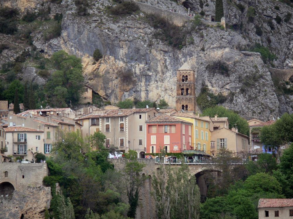 Guide de Provence-Alpes-Côte d'Azur - Paysages des Alpes-de-Haute-Provence - Village de Moustiers-Sainte-Marie : clocher de l'église Notre-Dame-de-l'Assomption, maisons, falaise (paroi rocheuse) et chemin de croix menant à la chapelle Notre-Dame-de-Beauvoir ; dans le Parc Naturel Régional du Verdon