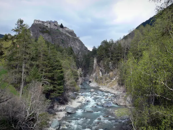 Regionaler Naturpark Queyras - Fort Queyras: Festung (Burg) in der Höhe sitzend auf ihrer felsigen Bergspitze überragend den Gebirgsbach Guil (Tal des Guil), Bäume am Wasserrand; in Château-Ville-Vieille