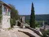 La Roque-sur-Cèze - Gepflasterte abfallende Gasse, Bildstock, Häuser, Zypressen und Kirchturm des Dorfes