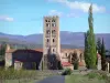 Saint-Michel de Cuxa abbey - Benedictine monastery, located in the town of Codalet, in Conflent: view of the abbey and its Romanesque bell tower with four stories from the road lined with orchards