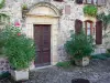 Sainte-Eulalie-d'Olt - Porte d'entrée d'une maison en pierre bordée d'arbustes en pots