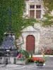 Sainte-Eulalie-d'Olt - Fontaine surmontée d'une croix, porte d'entrée et fenêtre à meneaux d'une demeure en pierre, et décorations florales de la cité médiévale