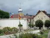 Salins-les-Bains - Koepel en lantaarn van de Notre-Dame-Liberator, het pad omzoomd met bloemen, bomen en huizen van het kuuroord