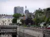 Segré - Passerelle enjambant la rivière Oudon, berge fleurie (fleurs), toit de l'Hôtel de Ville surmonté d'un lanternon, maisons et bâtiments de la ville