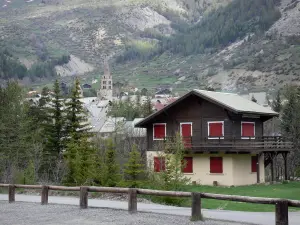 Serre-Chevalier - Serre-Chevalier 1500 (El Monetier-les-Bains), esquí (esquí): casa de campo en el primer plano, los árboles, torre de la Iglesia de Nuestra Señora de la Asunción y casas en el pueblo de Monêtier -les-Bains