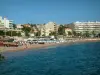 St. Raphael - Mar Mediterrâneo, praia de areia com visitantes de verão, guarda-sóis e espreguiçadeiras, palmeiras, casas e edifícios da estância balnear
