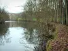 Suíça normanda - Orne Valley: árvores refletindo nas águas do rio, banco coberto com folhas mortas e viaduto ao fundo