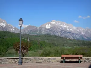 Valle del Champsaur - Farola y un banco en Saint-Bonnet-en-Champsaur, con vista a los árboles, los prados y en el fondo las montañas del Macizo del Dévoluy