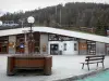 Vars - Vars-les-Claux, estação de esqui (estação de esportes de inverno e verão): praça decorada com chafariz de madeira e bancada, prédio que abriga o posto de turismo e árvores ao fundo