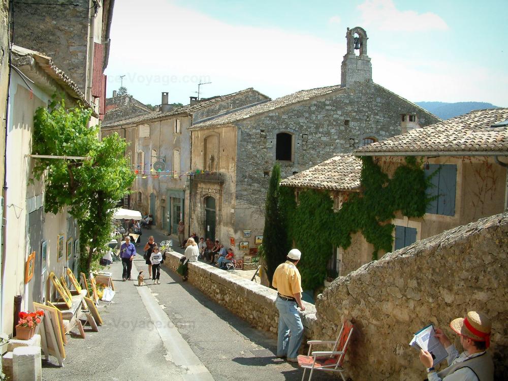 Guide du Vaucluse - Ménerbes - Rue du village avec des maisons et une exposition de tableaux
